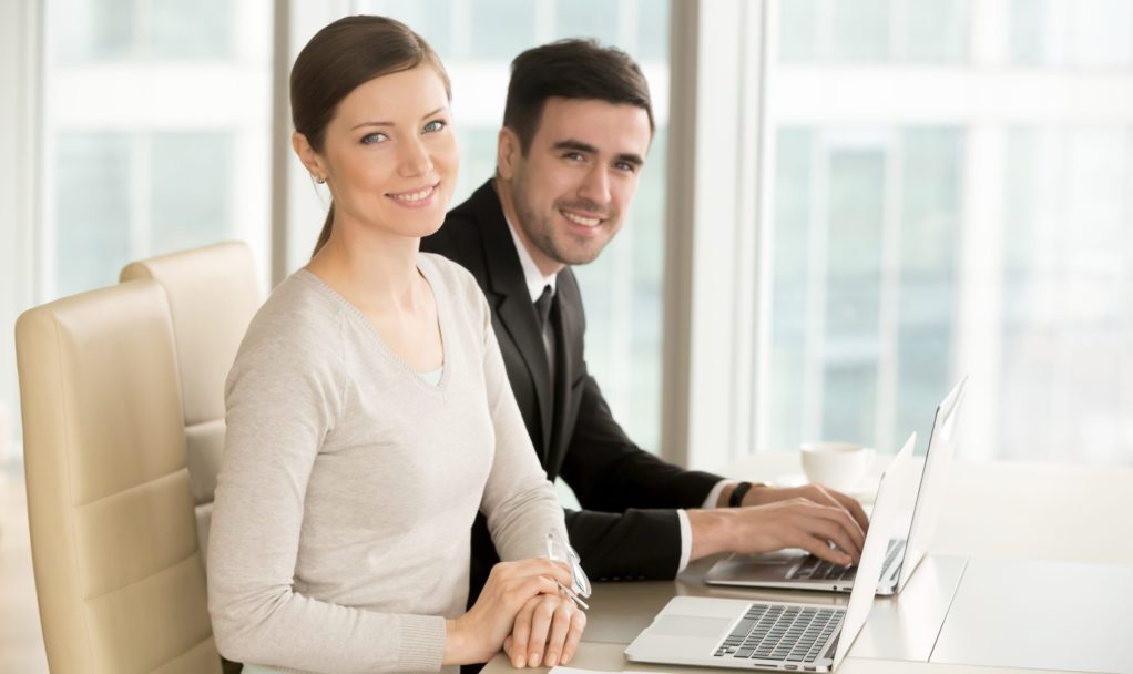 Smiling professional businesswoman and businessman with laptops Smiling professional businesswoman and businessman with laptops